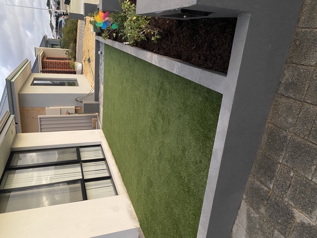 A tidy turf strip set into the same narrow side area, finished with crisp concrete edges and a small raised garden bed, after installation.