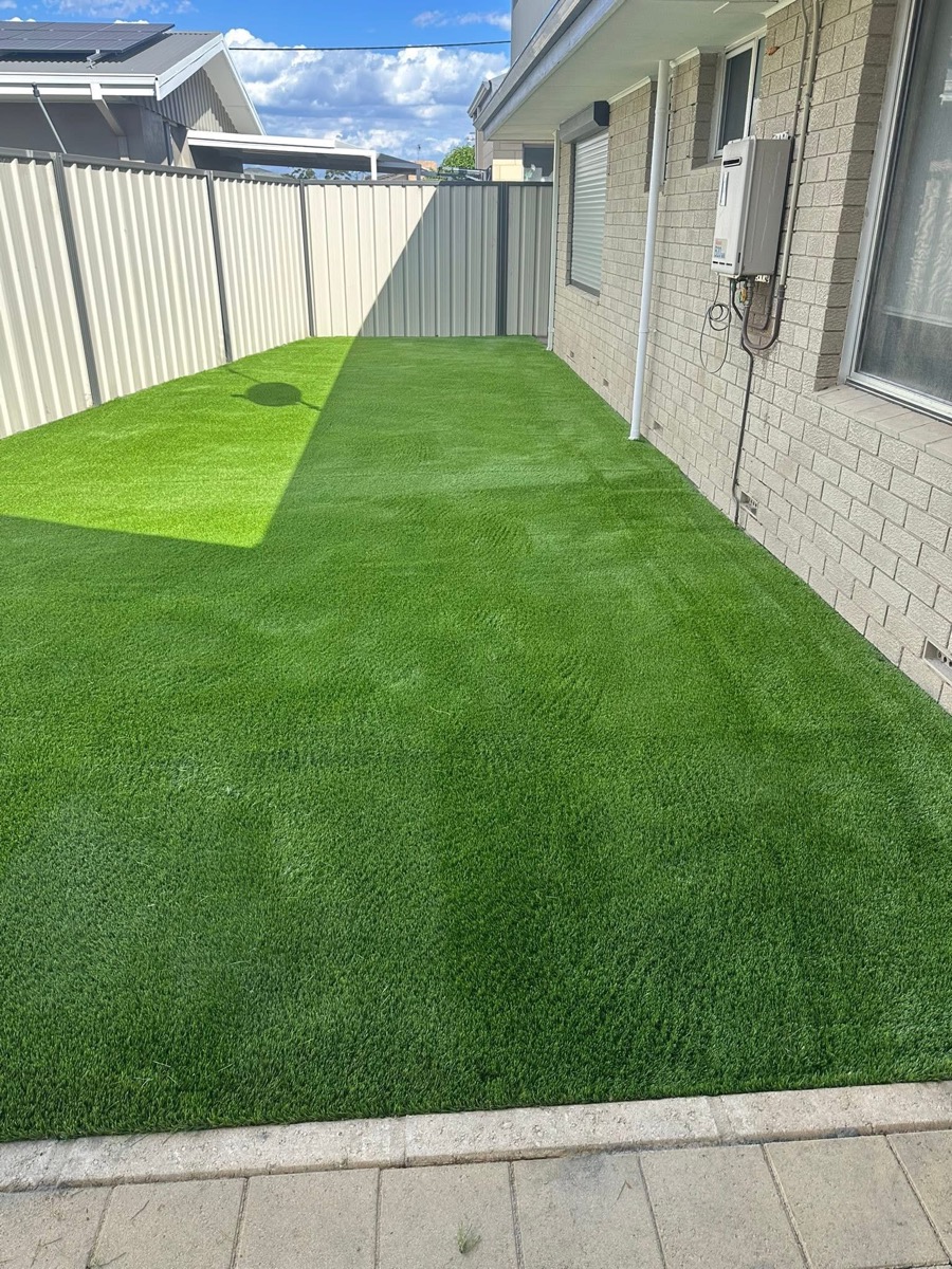 A finished backyard install with a full lush green artificial lawn, a brick paving border at the front, dark fencing along the back and a tidy edge against a brick home.